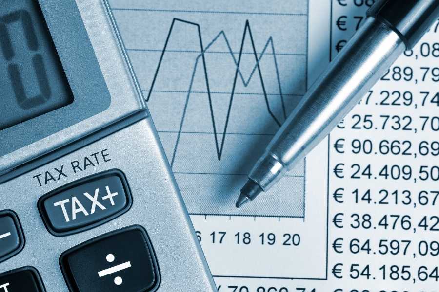 Une calculatrice avec une touche tax rate et un stylo posé sur un document financier rempli de chiffres.