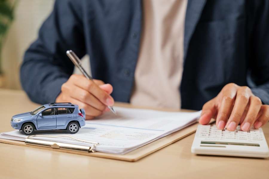 Une personne remplit des documents et calcule le coût de son assurance auto à l'aide d'une calculatrice.